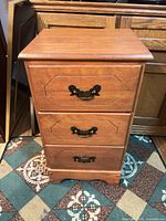Front view of medium brown three-drawer nightstand showing top, drawers with brass-tone pulls, and base
