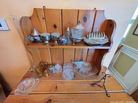Overall view of two-shelf pine rack containing silverplate pieces on upper shelf and pressed glass items on lower shelf