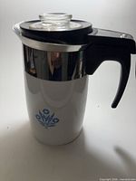 Full view of white electric percolator with blue floral motif and black handle