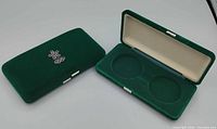 Two green velvet cases, one open showing dual coin recesses