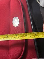 Front of red suitcase showing silver badge and measurement tape at 21 inches