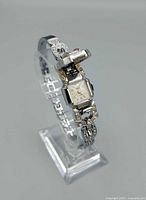 Side view of silver-tone wristwatch on stand showing band links and jeweled cover