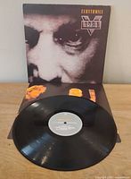 Front of jacket displayed upright behind vinyl record