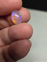 Oval crystal jelly opal held between fingers showing play-of-colour