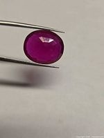 Oval faceted ruby held by tweezers showing table and crown