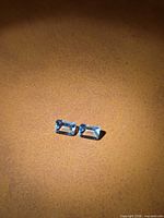 Two rectangular light blue gemstones on brown surface