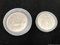 Obverse side of both coins in holders showing CANADA dollar voyageur design and coat of arms on 50 cent