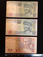 Three Ukrainian banknotes arranged vertically with ruler for scale