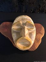 Front angled view of glazed ceramic grotesque face mask on wood base