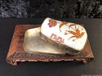 Closed box on stand showing porcelain shard lid with floral pattern
