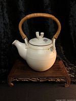 Front view of signed off-white glazed teapot on stand showing handle and spout