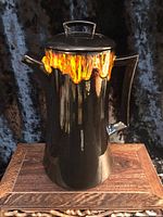 front view of black ceramic coffee pot with orange drip glaze and lid