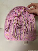 Front view of pink Baby Alive doll backpack showing logo, striped pocket, polka-dot fabric