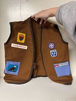 Front view of brown youth vest showing patches and pocket