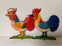 Front view of both colorful rooster figures on grass bases