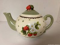 Left side view of ceramic teapot showing handle, spout, strawberry and flower relief