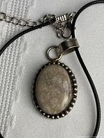 Close-up of pendant showing agatized coral cabochon and sterling silver beaded bezel on black cord