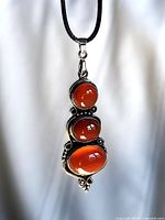 Front view of pendant showing three carnelian cabochons set in silver on black cord