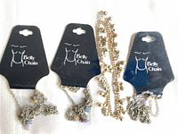 Three packaged silver-tone belly chains and one loose gold-tone ankle bell chain displayed on fabric