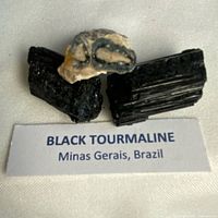 Three Black Tourmaline pieces displayed on cloth with label showing origin