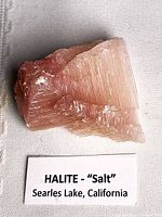 Front view of pink halite crystal on cloth background with label