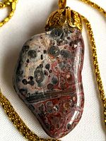Front view of polished leopard skin jasper pendant with gold-tone cap on chain