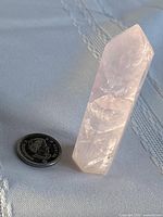 Rose quartz point beside coin for scale, angled view