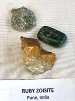 Three ruby zoisite specimens on fabric background with identifying label
