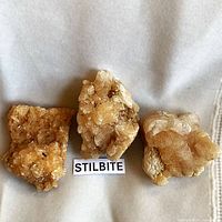 Three stilbite clusters on light fabric background with label
