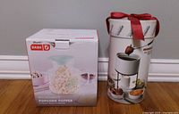 Front view of boxed Dash microwave popcorn popper beside boxed fondue set