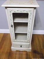Front view of painted cabinet showing glass door, vine motif, lower drawer