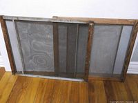Two vintage wooden window screens leaning against wall