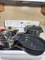 Group view of all pots and lids on stove including graniteware pieces and stainless saucepans