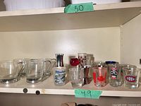 Shelf view showing six handled cups left, various shot glasses and jigger right