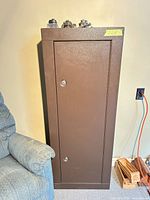 Front view of brown hunting safe cabinet beside chair, full height visible