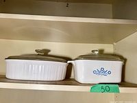 Two small CorningWare casserole dishes on shelf, each with lid