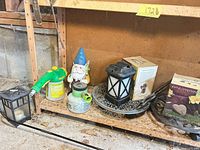 Shelf with gnome, sprayers, lantern, plant caddy, boxed memorial stone