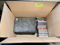 Cardboard box with stack of jewel-case CDs and black Case Logic carrying case