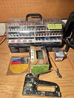 All items grouped on workbench: staple gun, rotary accessory kit, screw boxes, sanding discs, seam roller