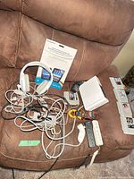 Wii console vertical with controllers, headphones, NES cartridges, cables on couch