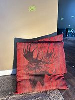Front view of both red moose print pillows leaning against wall