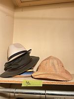 Three hats on shelf: white felt fedora over olive canvas outback; tan straw safari hat beside