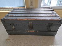 Front view of closed gray wooden trunk with slatted lid and metal latches