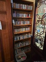 Full height view of wooden bookcase shelves filled with CDs and plastic tub with loose discs at bottom