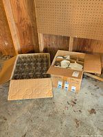 Two cardboard boxes on floor, one open showing jars arranged, second box partially open