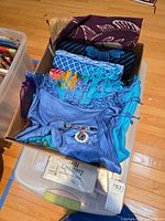 Cardboard box of fabric scraps with scissors and measuring tape inside plastic bin