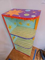 Front angled view showing painted top with stars and planets, shelf fronts