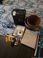 All items together on rug: shredder, trimmer, baskets, boxed drive, rulers, tape, pens