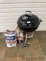 Grill with attached legs and wheels next to charcoal bags
