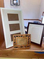 three frames: white triple-opening, brown matted, carved wood tabletop